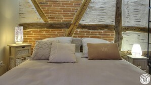 A bedroom with a brick wall, wooden beams, a bed with white bedding, and bedside lamps. - la Ferme aux Colombages (MARBOZ)
