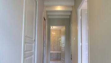 Un pasillo con puertas blancas, piso de baldosas y techo con vigas a la vista.