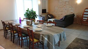 A dining area with a table set for six, surrounded by wooden chairs. A potted plant is on the table, and a television is mounted on the wall.