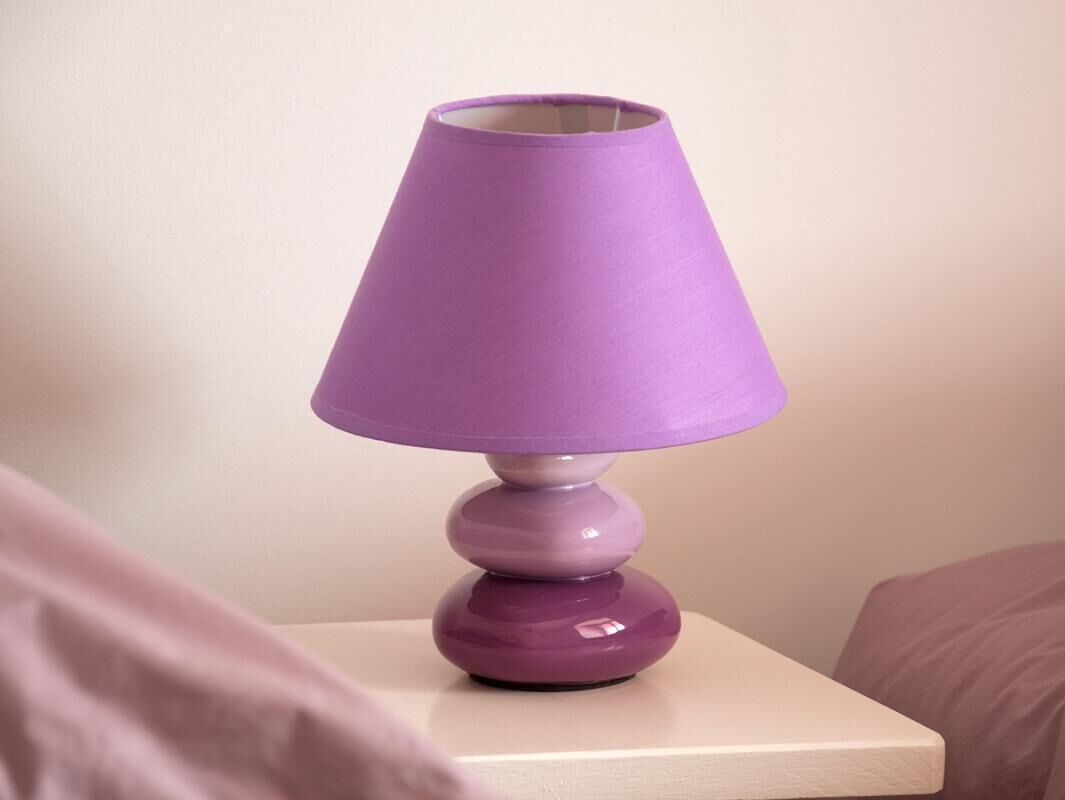 Une lampe de chevet violette posée sur une table de chevet blanche.