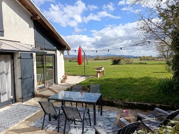 A patio with a glass table and chairs, a red umbrella, and a view of a grassy field.