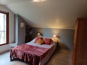 Ett sovrum med en säng, två sänglampor, ett nattduksbord, ett fönster och en garderob i trä.