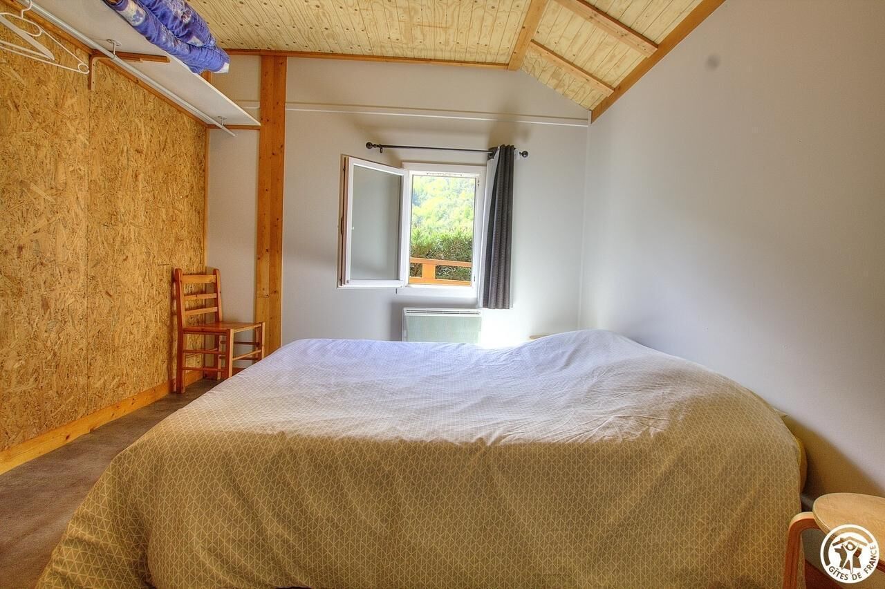 A bedroom with a bed, a chair, a window with curtains, and a view of greenery outside.
