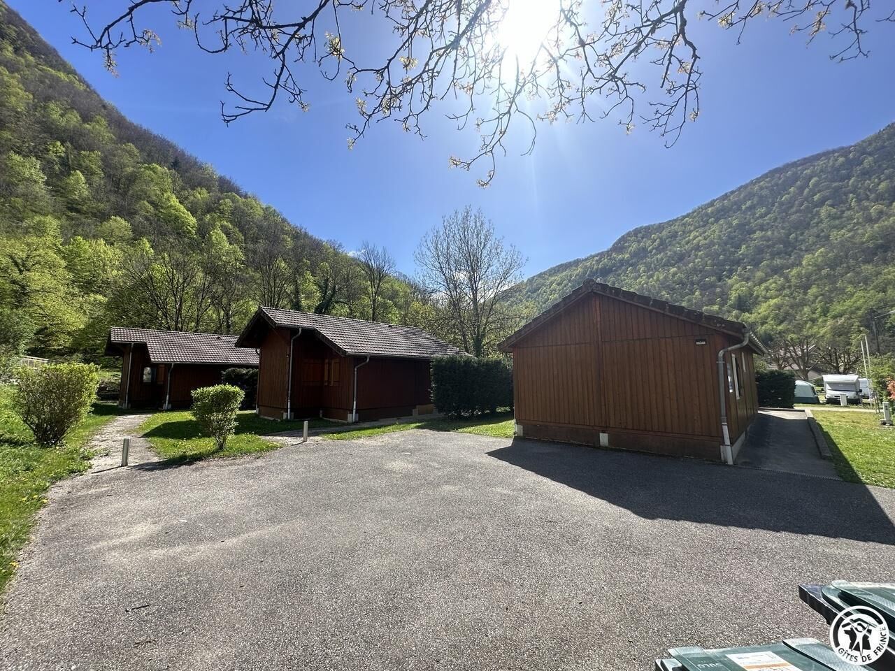 A rural property with a gravel driveway leading to a wooden building, surrounded by lush greenery and hills.