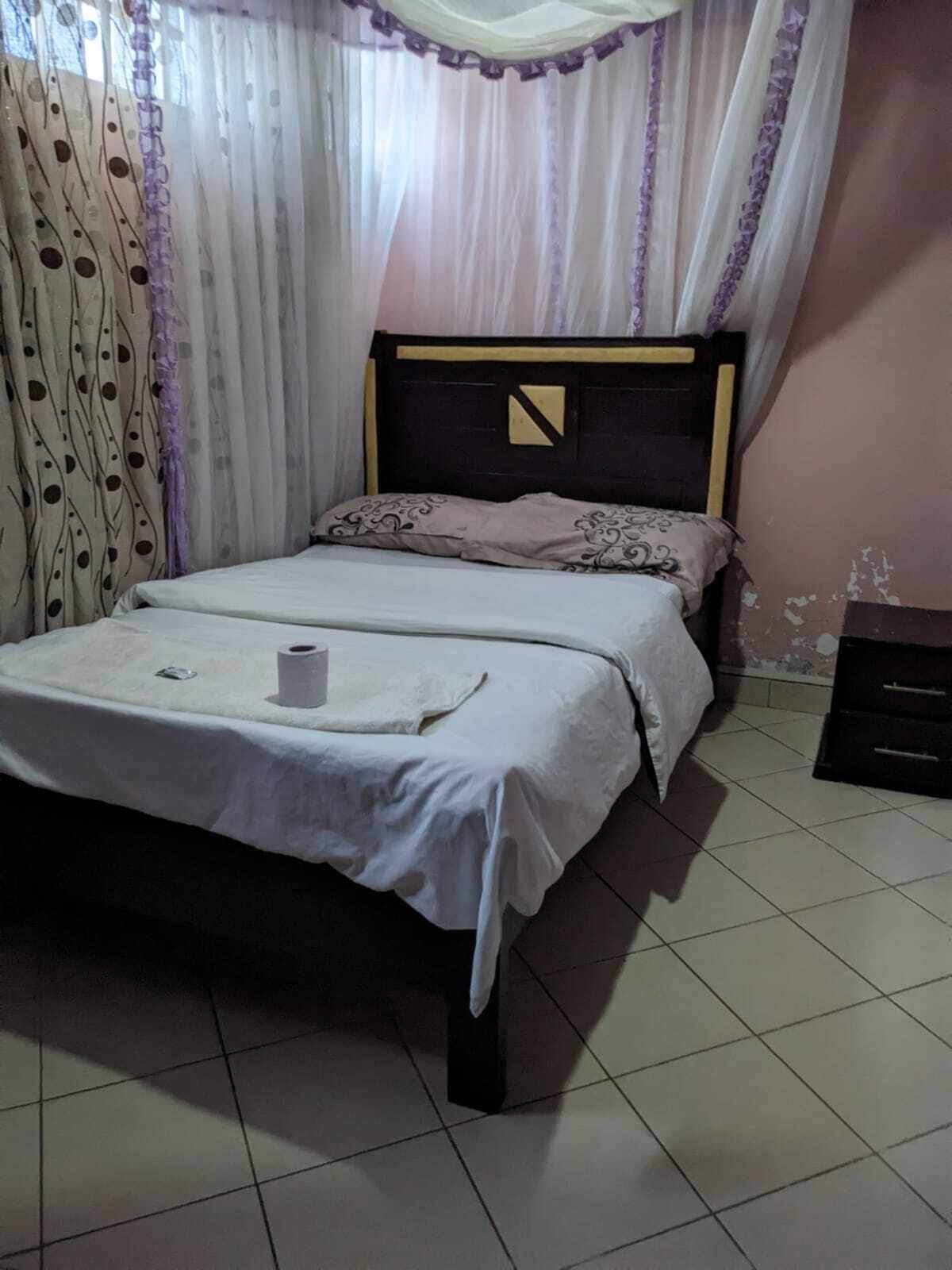 A bed with a white bedspread and a single pillow, a small bedside table, and a curtain with a leaf pattern.