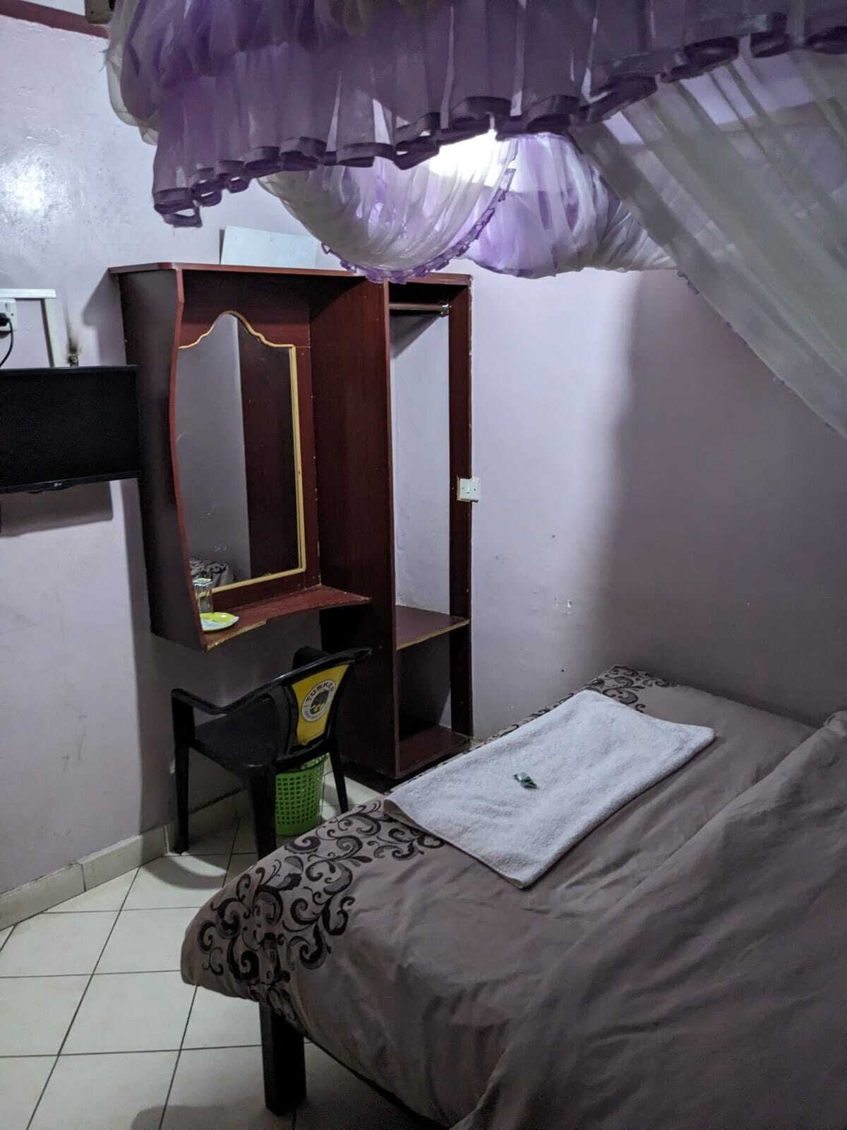 A bedroom with a bed, a desk with a chair, a wardrobe, and a purple canopy.