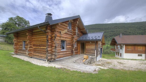 A log cabin with a wooden exterior, a front porch, and a small attached building. - Chalet La Fuste Monts Jura (LELEX)