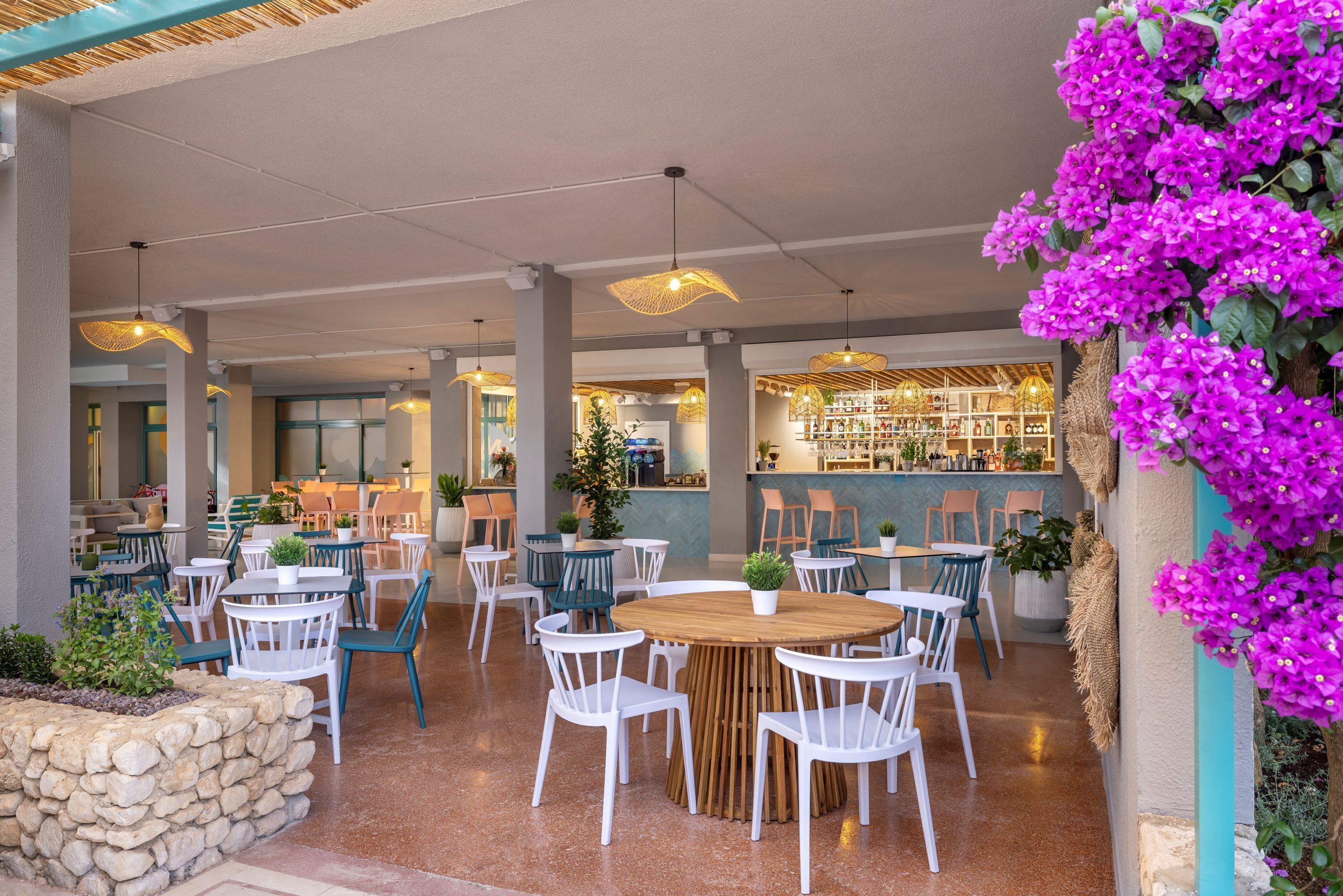 Un espace extérieur aménagé avec des tables rondes en bois et des chaises blanches, entouré de murs en pierre et agrémenté de plantes en pot.