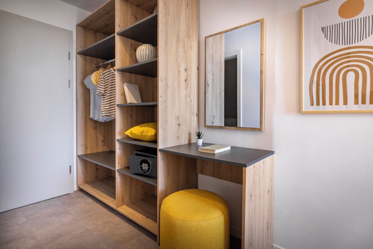 Une chambre moderne avec une armoire en bois, un petit bureau et un pouf jaune.