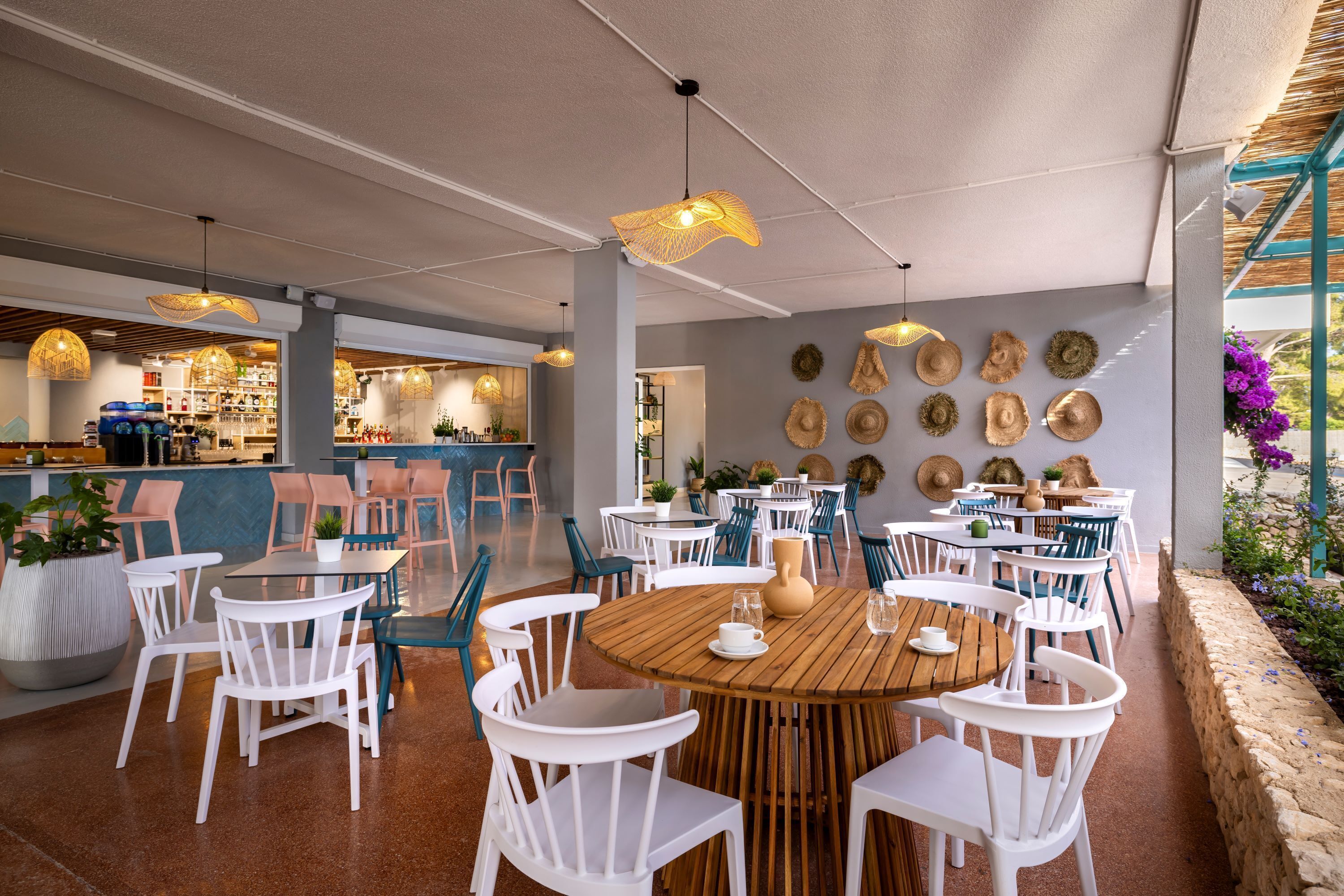 Un restaurant avec des tables rondes en bois et des chaises blanches, un coin bar et un mur décoré de chapeaux.