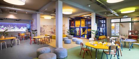 A spacious indoor area with multiple tables and chairs, featuring a play area with colorful furniture and a large aquarium.