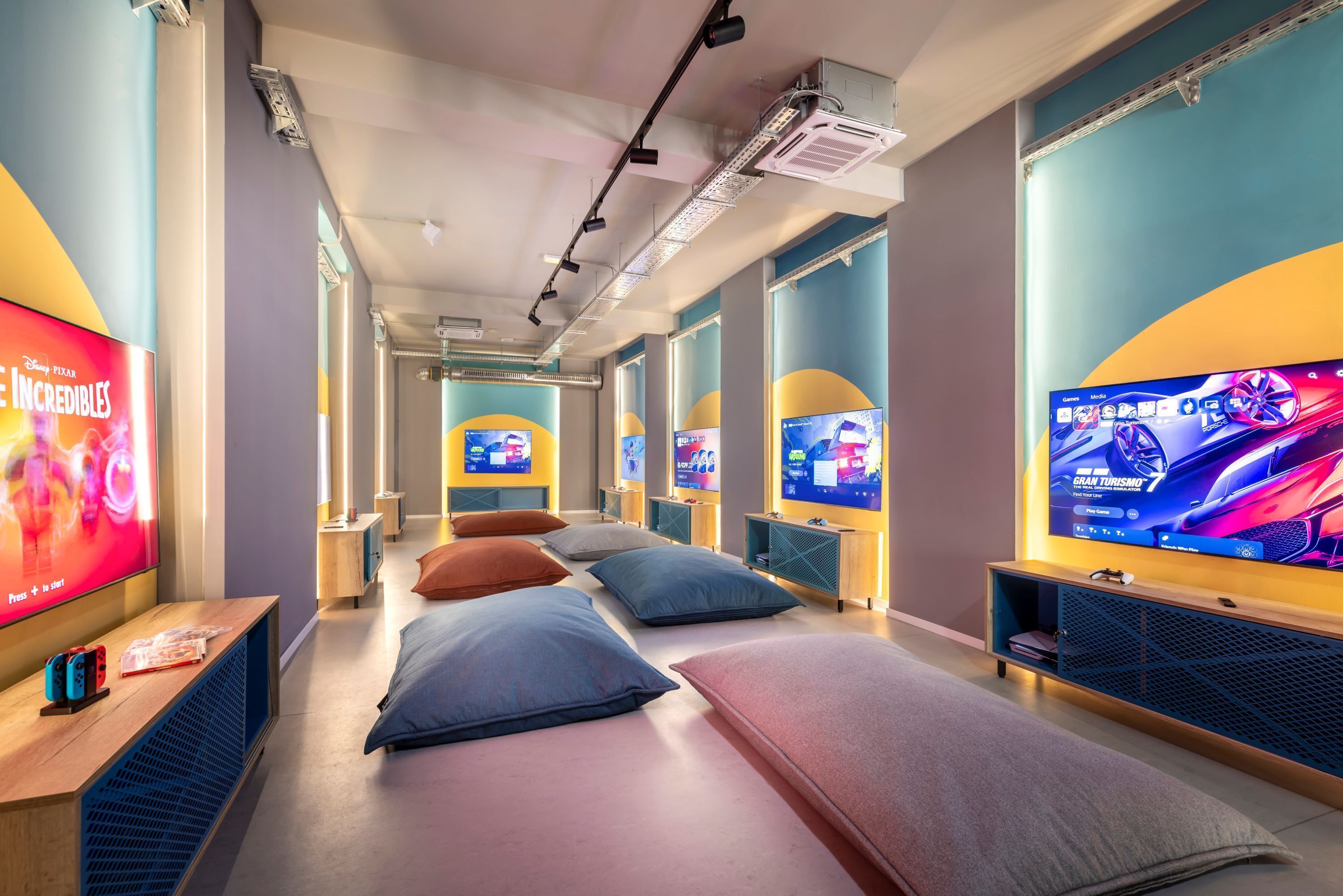 A hotel room with a large TV screen, multiple beds, and a gaming console.