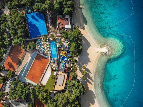 An aerial view of a resort with a beach, a tennis court, and a pool area.