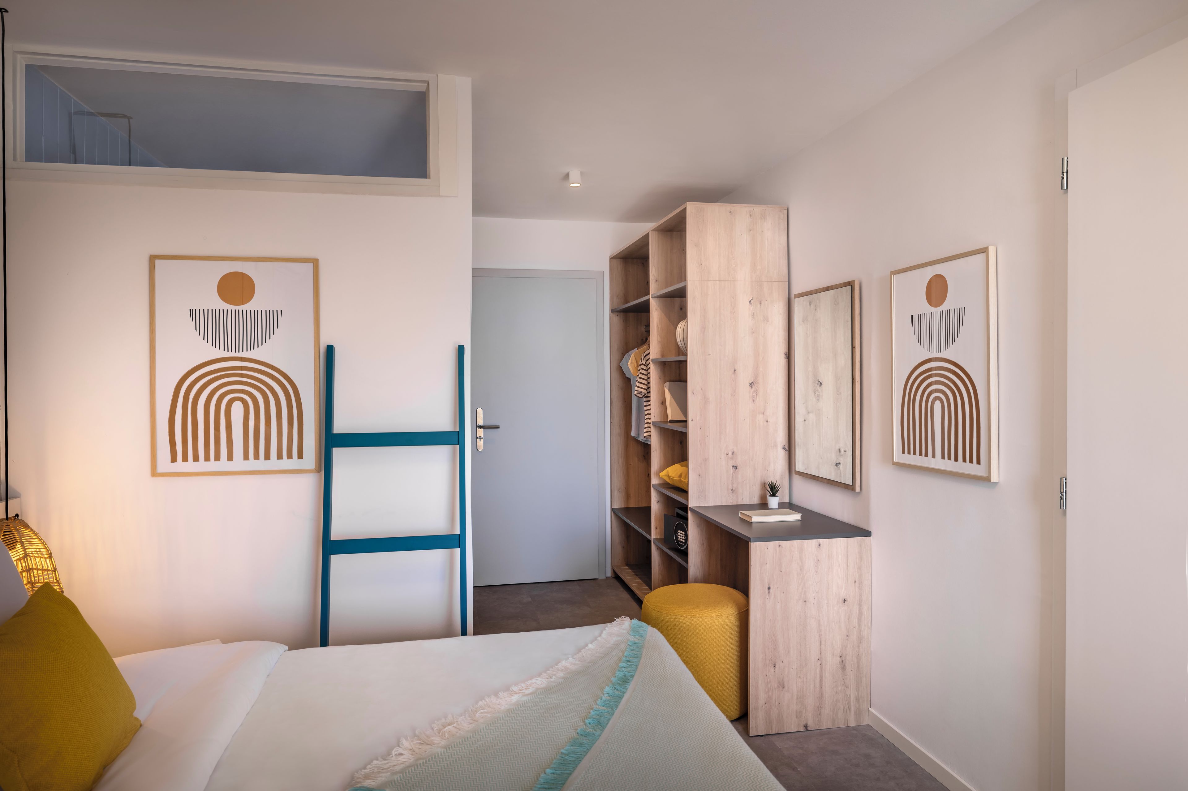 A bedroom with a bed, a desk, a wardrobe, and two framed artworks.
