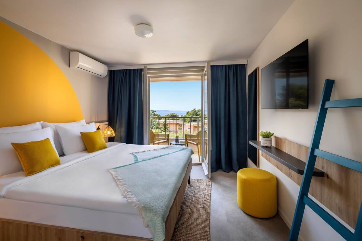 Une chambre d’hôtel moderne dotée d’un grand lit, d’une télévision, d’un balcon avec vue et d’un bureau avec une chaise.