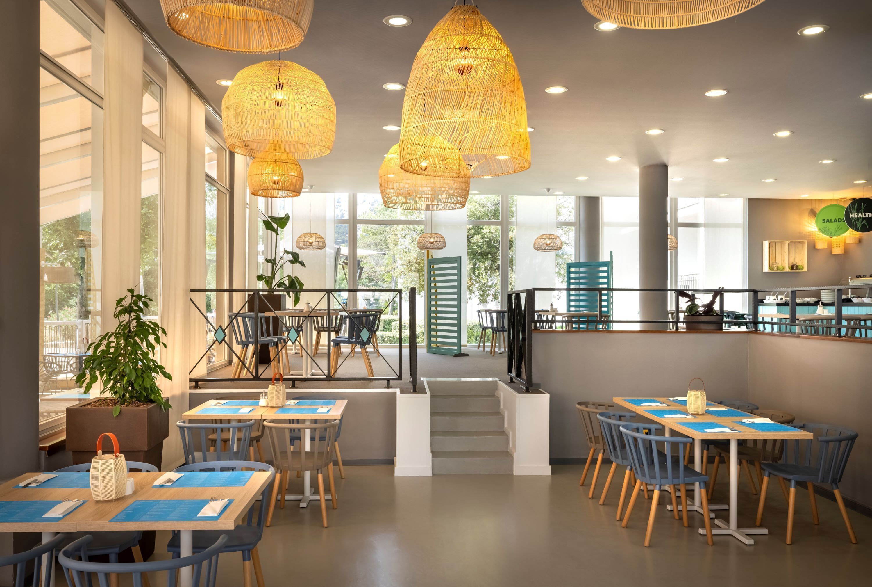 A modern restaurant interior with high ceilings, wicker pendant lighting, and a staircase leading to an outdoor area.