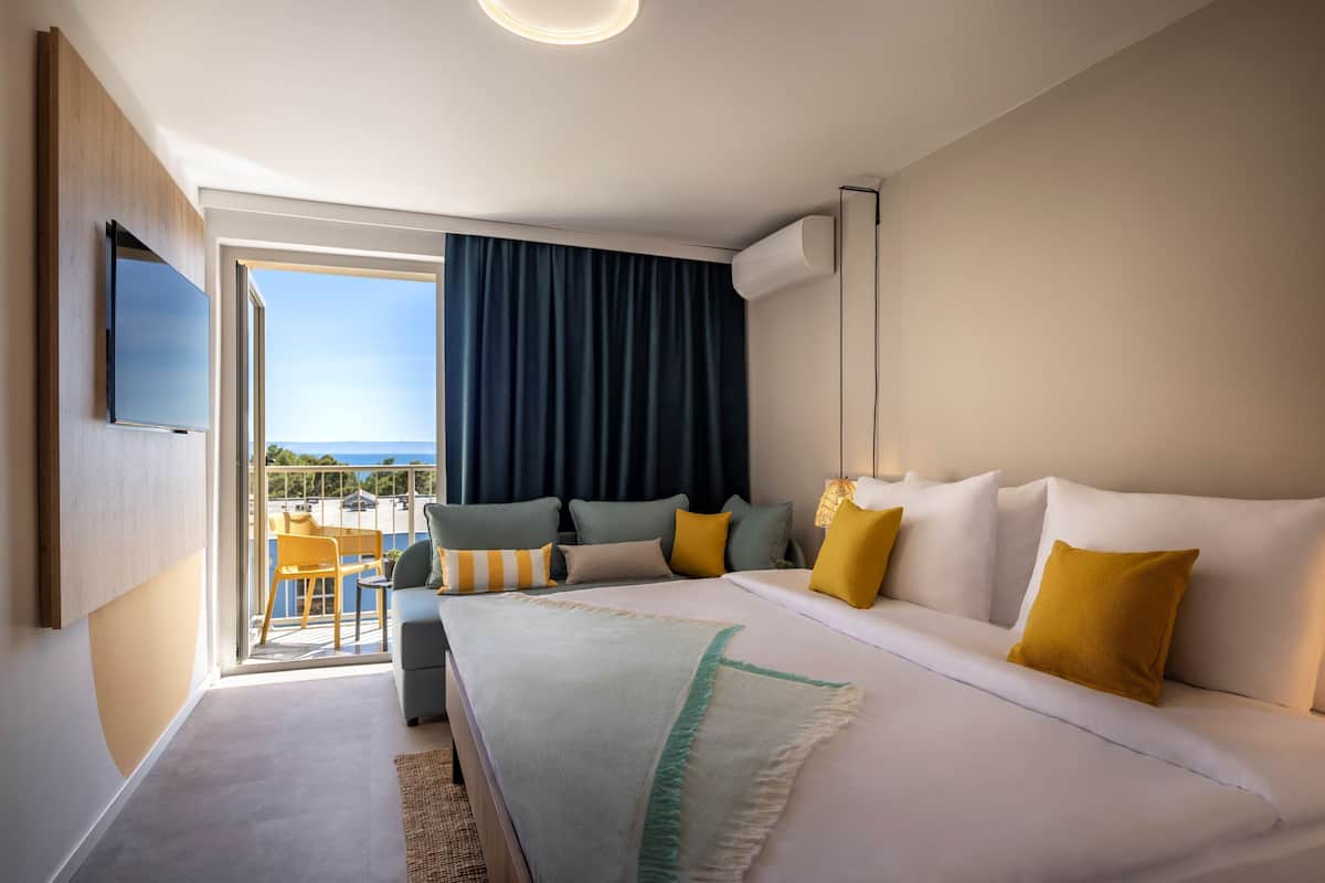 Une chambre d’hôtel moderne dotée d’un grand lit, d’un téléviseur fixé au mur et d’un balcon offrant une vue sur la mer.