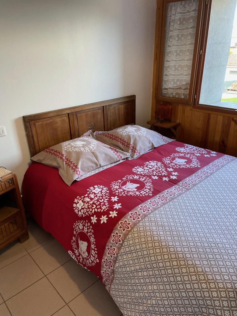 Un lit avec une tête de lit en bois, une couvre-lit à motifs rouges et blancs, et une fenêtre avec un rideau.