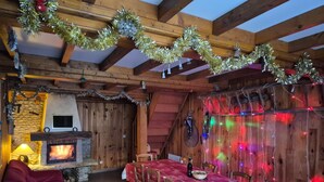 Een gezellige kamer met een open haard, houten balken, een eettafel met stoelen en feestelijke decoraties.