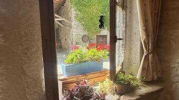 Quarto rústico com parede de pedra, moldura de janela de madeira e vista para um jardim com flores e uma parede verde.