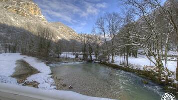 Ein Fluss, der durch eine verschneite Landschaft fließt, mit kahlen Bäumen und einer felsigen Klippe im Hintergrund.