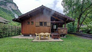 Una cabaña de madera con balcón, antena parabólica y una mesa con sillas en el patio.