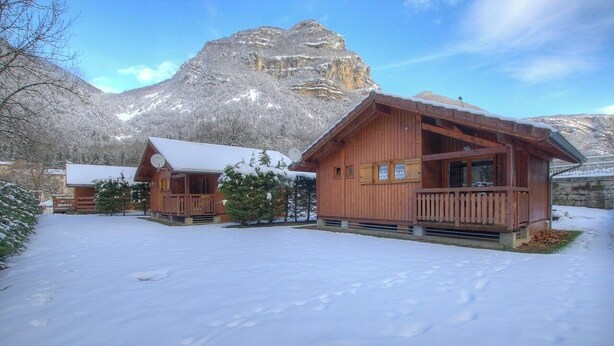 Una cabaña de madera con balcón, con una imponente montaña nevada de fondo.