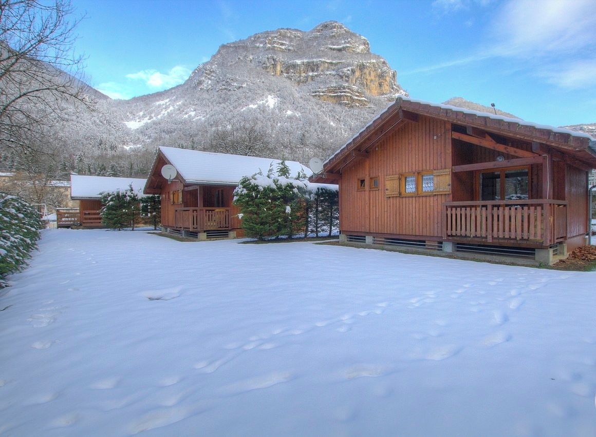 Una cabaña de madera con balcón, con una imponente montaña nevada de fondo.