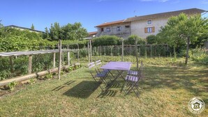 A garden with a table and chairs, a pergola, and a house in the background.