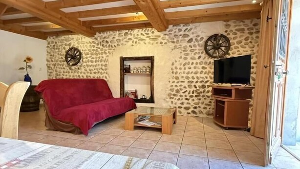 A cozy attic room with a bed, a red sofa, a TV, and a stone wall.
