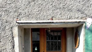 A small, rustic building with a wooden door and a window with a metal grill.