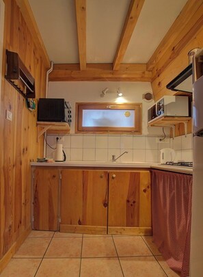 Eine kleine Küche mit Holzausstattung, einer Mikrowelle, einem kleinen Fenster und einem Fliesenboden.