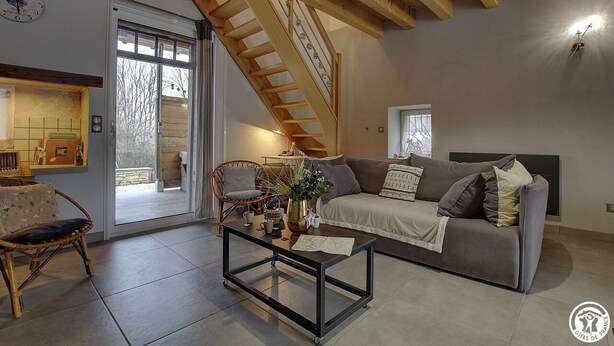 A living room with a sofa, coffee table, wicker chair, and a staircase. - des Grands Cours - Marboz (MARBOZ)