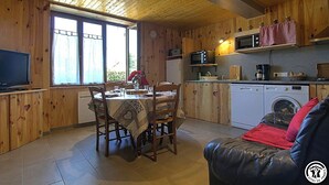 Um quarto acolhedor em estilo cabana, com uma mesa de jantar, cadeiras, um sofá, uma televisão, micro-ondas, máquina de café e máquina de lavar roupa.