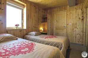 A wooden-paneled room with two beds, a window with a vase of flowers, and a door.