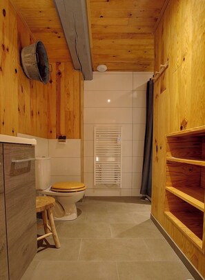 A wooden-paneled bathroom with a toilet, a small stool, and a shelf unit.