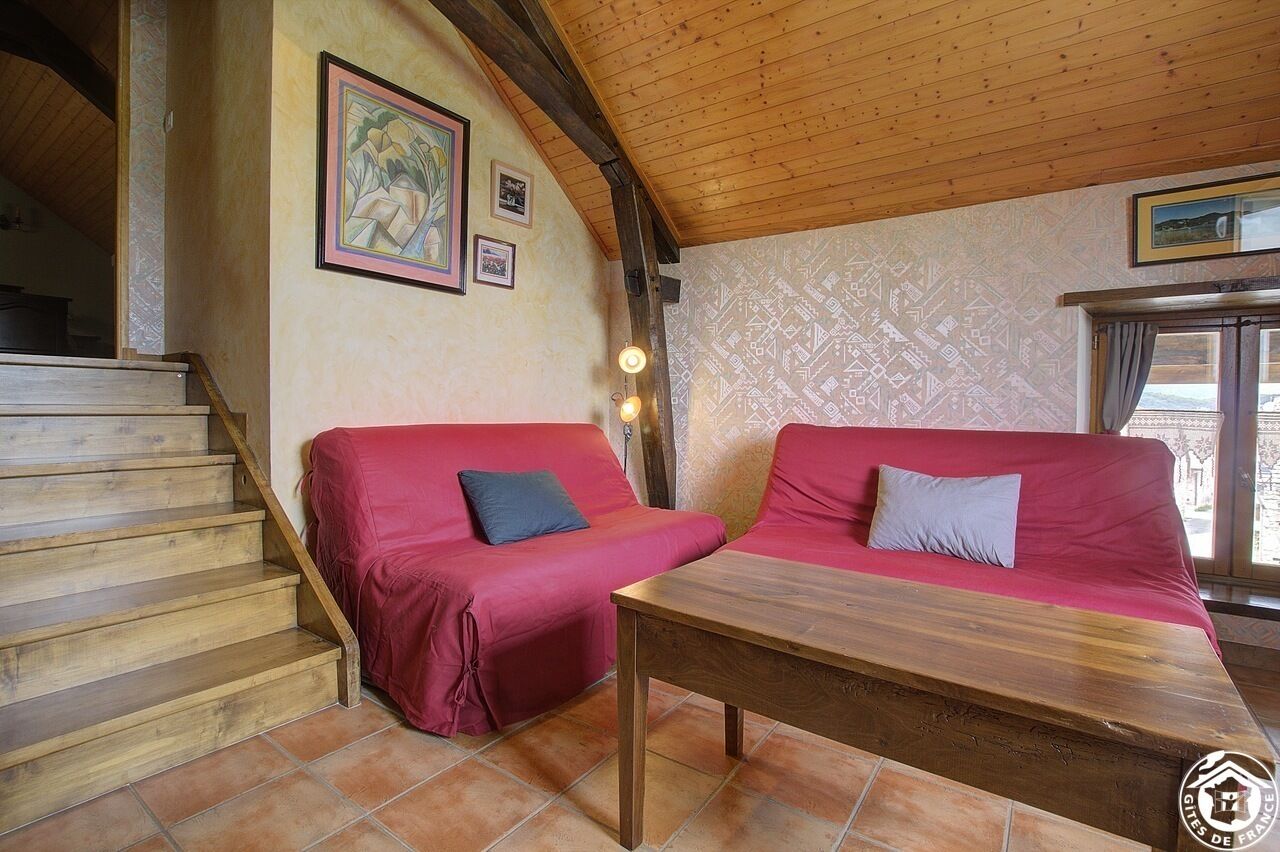 A room with a wooden staircase, two red sofas, a wooden table, and patterned wallpaper.