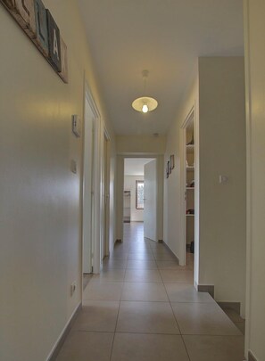 A hallway with a light fixture, a door, and a shelf with items.