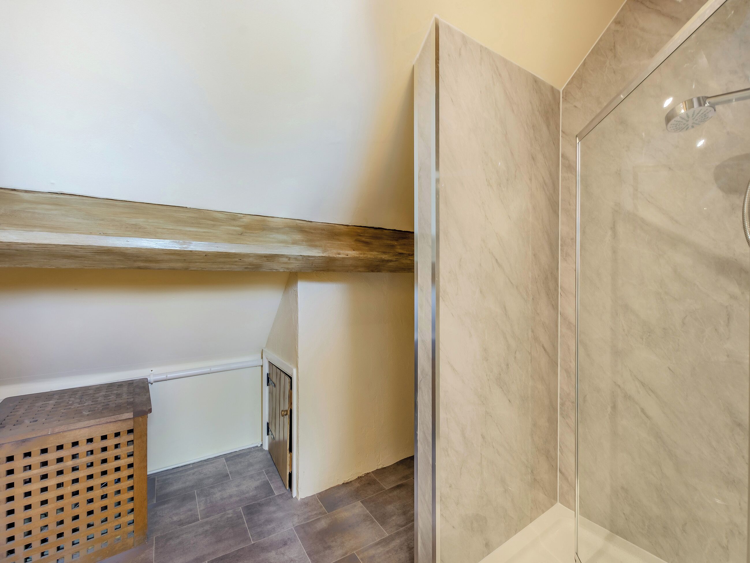 A modern bathroom with a shower, wooden beam ceiling, and grey tiled floor.