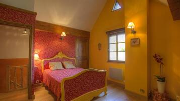 Une chambre avec un lit en bois, une couvre-lit à motifs floraux rouges et un mur jaune.