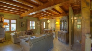 A spacious living room with a high wooden ceiling, a dining area with a table and chairs, and a kitchen with wooden cabinets and a built-in oven. - Les Epées - Conzieu - Gîte (CONZIEU)