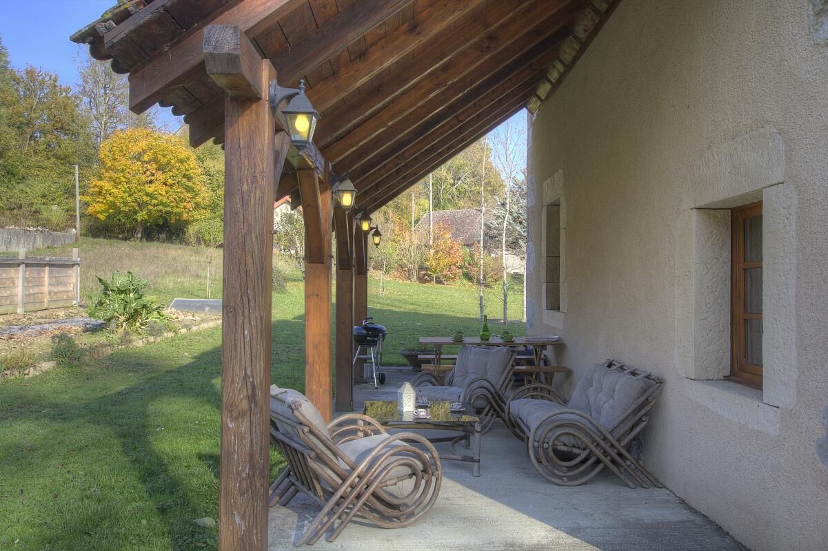 Een overdekt terras met rieten meubels, een tafel en een barbecuehoek.