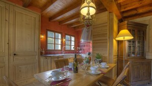 A wooden dining table set with white plates, glasses, and cutlery, a bottle of wine, and a vase with flowers. - Les Epées - Conzieu - Gîte (CONZIEU)