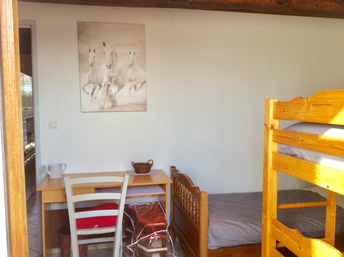 A bunk bed, a desk with a chair, a painting of horses, and a small table with a basket.