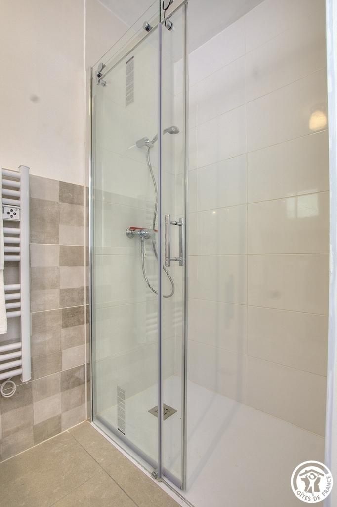Een douche met glazen wand, bedieningspaneel, handdoekhouder en een wand van zwart-witte tegels.