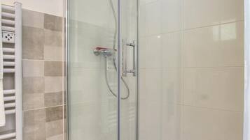 Een douche met glazen wand, bedieningspaneel, handdoekhouder en een wand van zwart-witte tegels.
