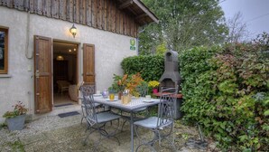 A rustic building with a wooden exterior, a patio with metal chairs and a table, and a brick oven.