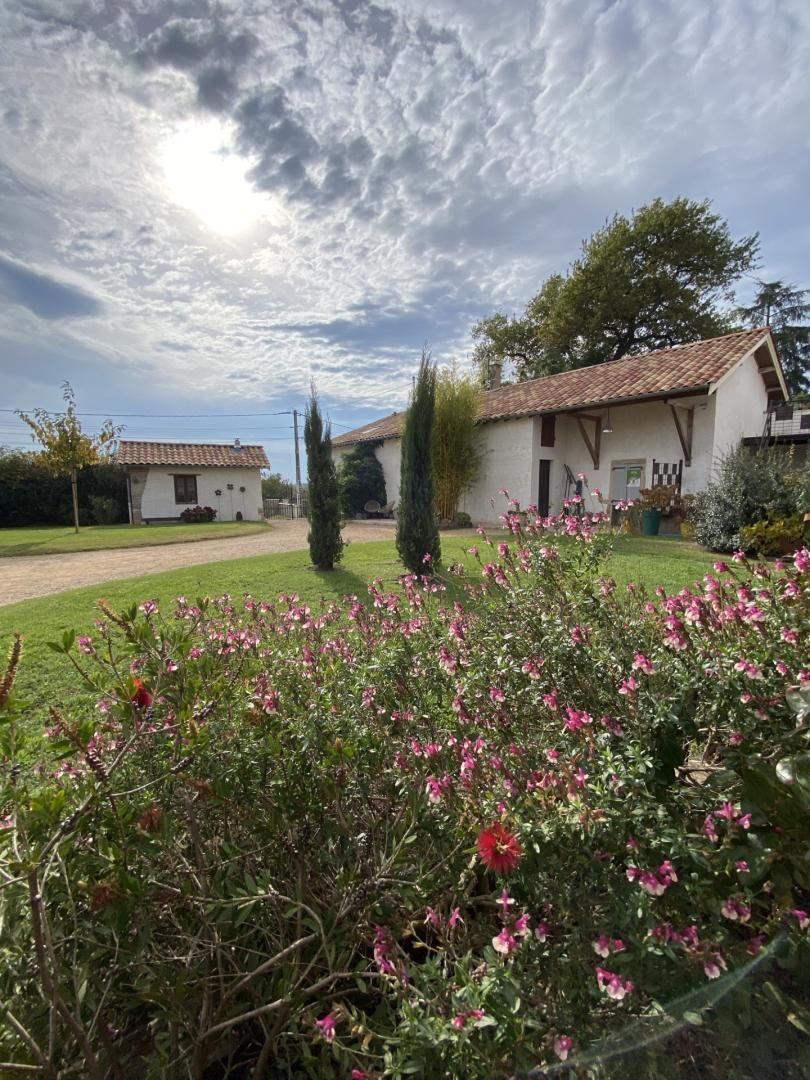Ein ländliches Haus mit Ziegeldach, umgeben von einem gepflegten Garten mit rosa Blumen und einer Rasenfläche.