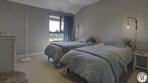 A bedroom with two beds, a window with curtains, a floor lamp, and a bedside table. - Lacooldouss - Druillat (DRUILLAT)