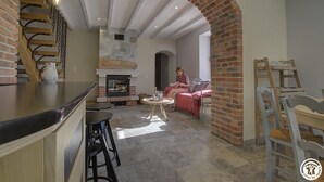 A cozy interior with a brick fireplace, a wooden staircase, and a seating area with a table and chairs. - Lacooldouss - Druillat (DRUILLAT)